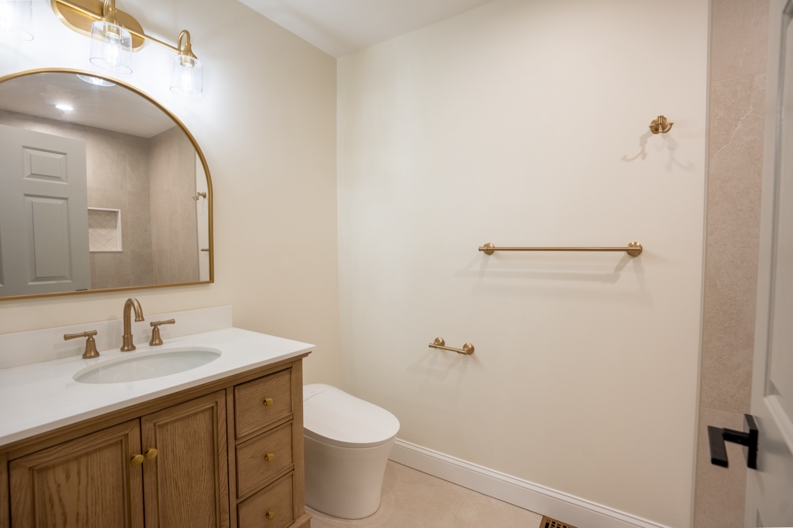 Bathroom with oak vanity, arched mirror and brass fixtures