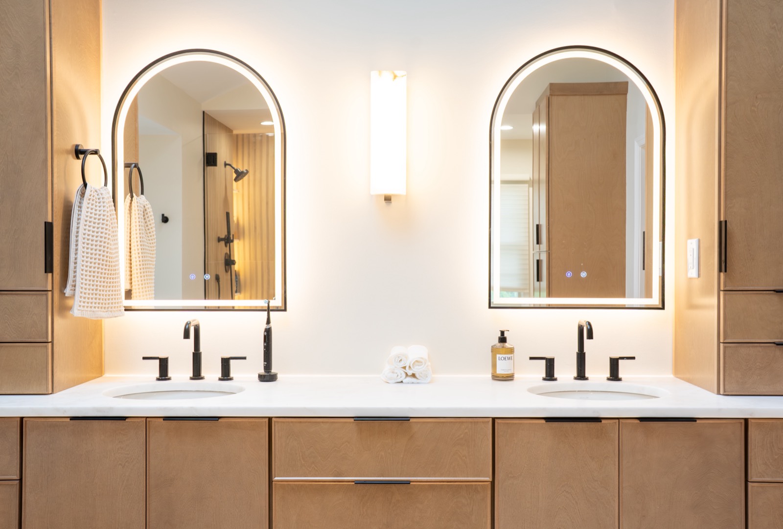 Double vanity with arched backlit mirrors and wood cabinetry